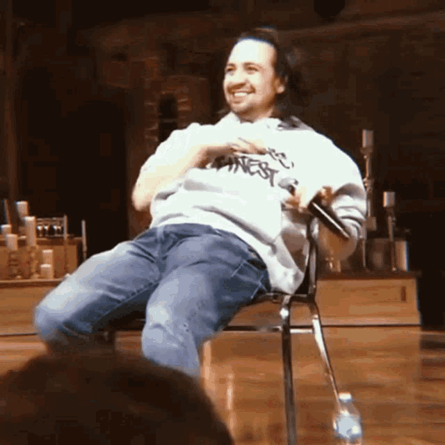 a man wearing a sweatshirt that says honest is sitting in a chair holding a microphone
