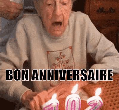 an elderly woman is blowing out candles on a birthday cake with the words bon anniversaire written on the bottom .