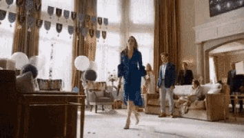 a woman in a blue dress walks through a living room