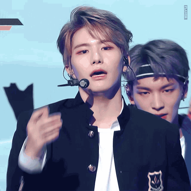 a man wearing a headband and a microphone stands in front of another man wearing a jacket