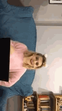 a woman in a pink sweater is sitting on a blue couch with a laptop on her lap
