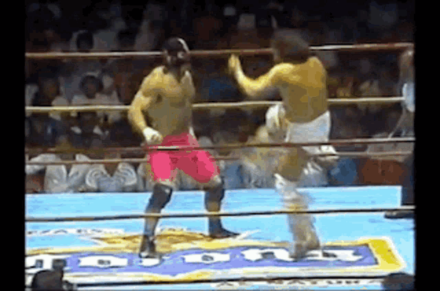 two men are wrestling in a boxing ring with a sign that says ' tnt ' on it .
