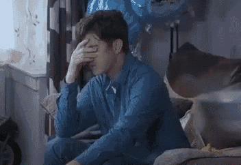 a man in a blue shirt is sitting on a couch with his hand on his forehead .
