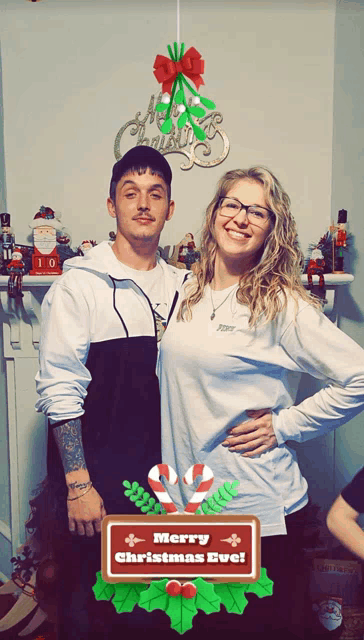 a man and a woman pose for a picture with a merry christmas eve sign in front of them