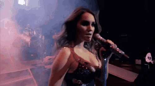 a woman is singing into a microphone on a stage in a dark room .