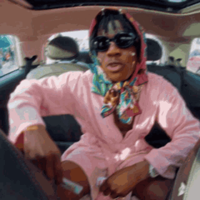 a woman in a pink robe and scarf is sitting in a car