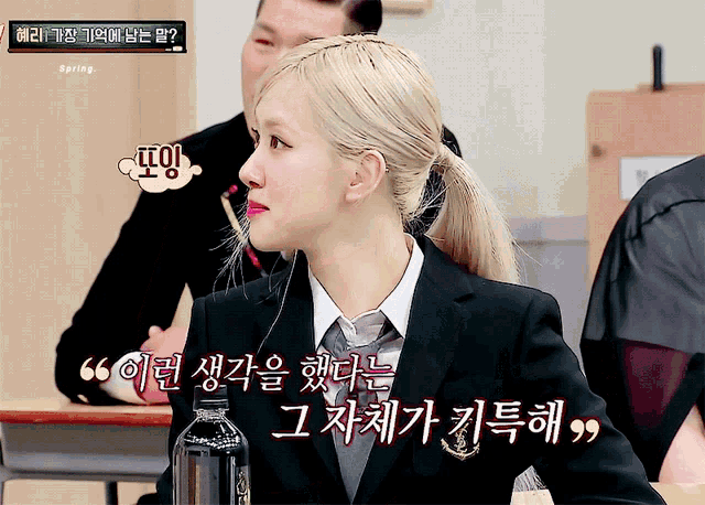 a woman in a suit and tie is sitting at a desk with a bottle of water