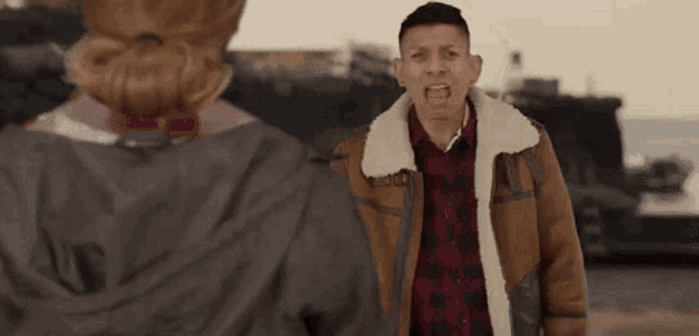 a man in a brown jacket is standing next to a woman in a plaid shirt .