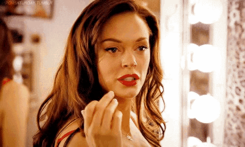 a woman is applying lipstick in front of a mirror in a room .