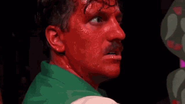 a man with red paint on his face is wearing a green shirt and a green jacket .