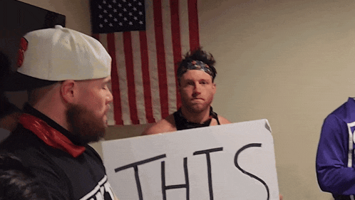 a man holding a sign that says thts stands in front of an american flag