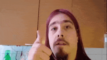 a man with long pink hair and a beard is giving a thumbs up .
