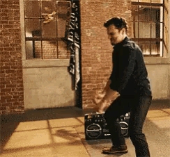 a man is dancing in front of a boombox in a room with brick walls .