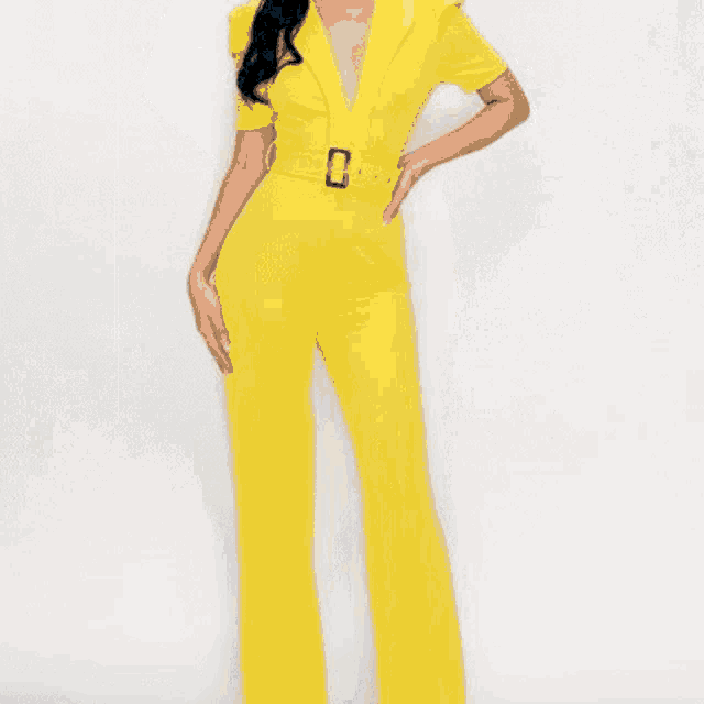a woman is wearing a blue denim jumpsuit with a belt and heels .