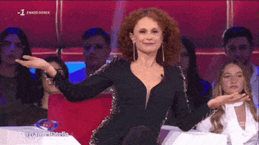 a woman in a black dress is sitting in front of a crowd with the words ennio dores on the screen behind her