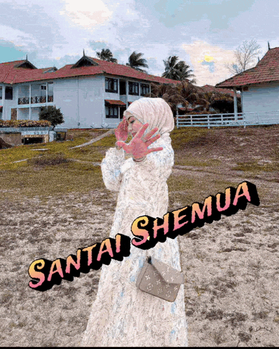 a woman wearing a hijab is standing on a sandy beach with the words santai shemua written on the bottom