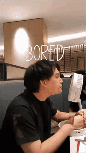 a man sitting at a table with the word bored written above him