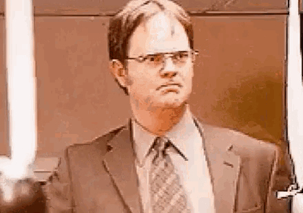 a man in a suit and tie is standing in front of a door and looking at the camera .