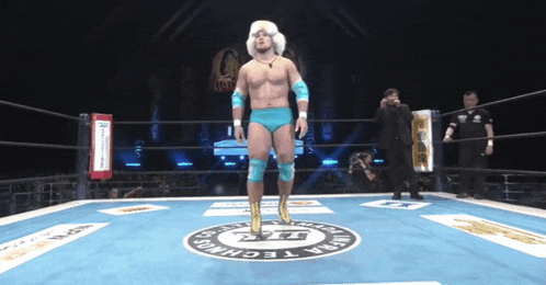 a wrestler is standing in a ring with a t.t. logo on the ground