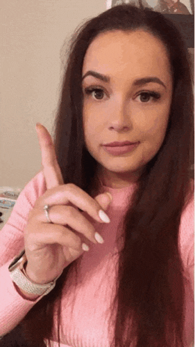 a woman wearing a pink sweater and white nails is pointing up