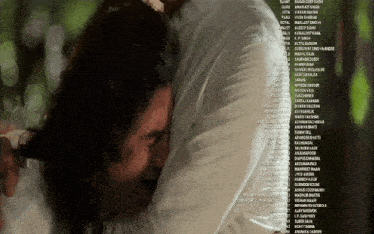 a man with long hair is hugging another man with a list of names behind him