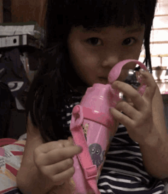 a little girl is drinking from a pink water bottle with an octopus on it