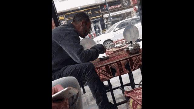 a man sits at a table with plates on it in front of a burger king store