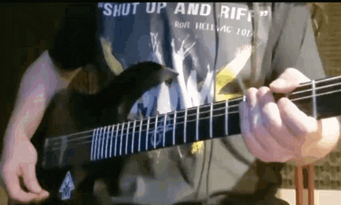 a man wearing a shirt that says " shut up and riff " is playing a guitar