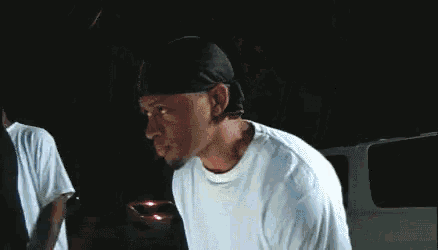 a man wearing a black hat and a white shirt is standing in front of a car .