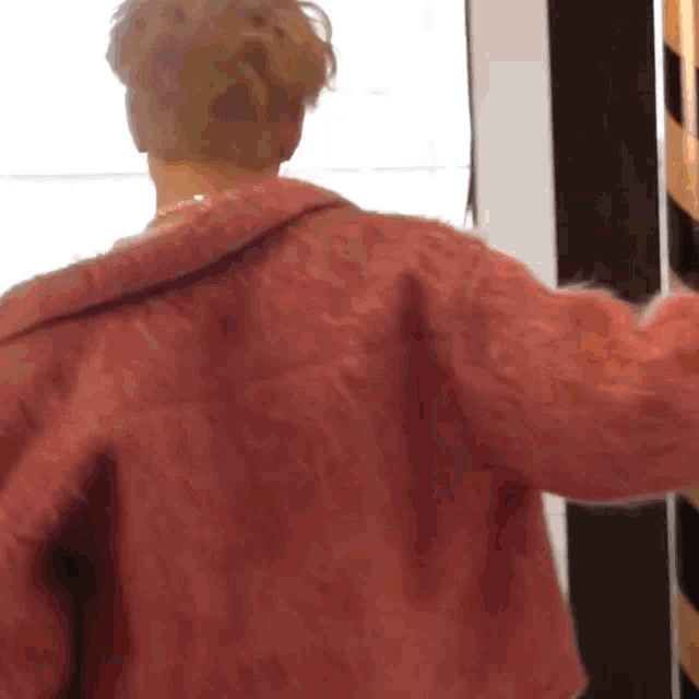 a woman in a pink coat is standing in front of a window with her arms outstretched .
