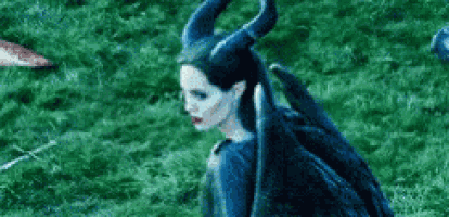 a woman with horns and wings is sitting in the grass .