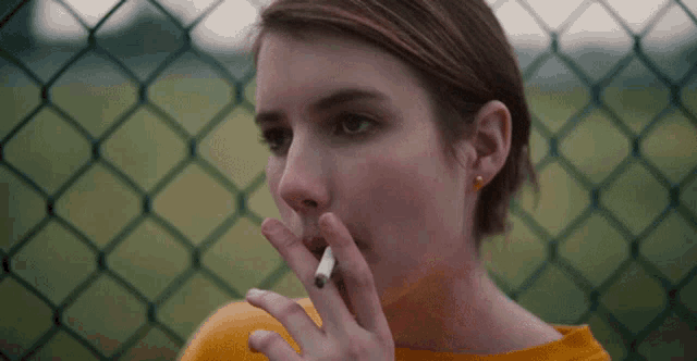a woman in a yellow shirt is smoking a cigarette