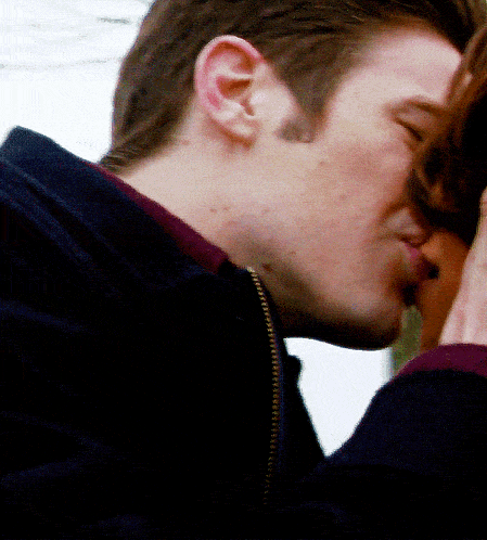 a man in a black jacket kisses a woman in a purple shirt