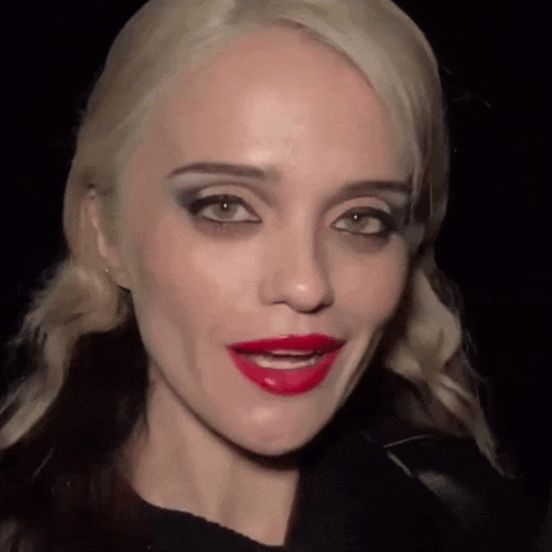 a woman with blonde hair and red lips looks at the camera