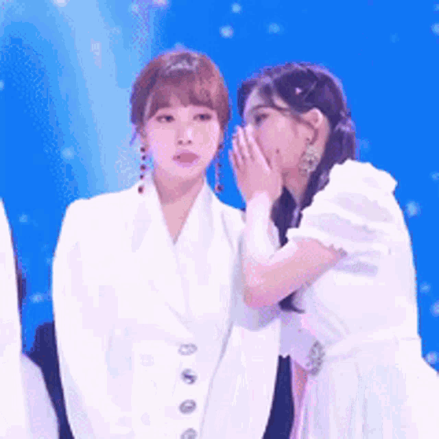 a woman whispering into another woman 's ear while standing next to each other
