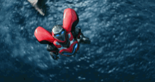 a red and black robot is flying through the air over a body of water