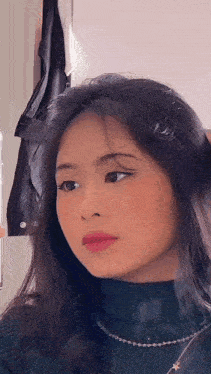 a woman is looking at herself in the mirror while wearing a turtleneck sweater and a necklace .