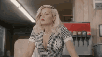 a woman in a plaid dress is standing in front of a soda machine .