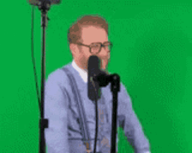 a man in a blue shirt and tie is standing in front of a green screen .