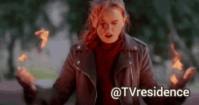 a woman in a leather jacket is standing in front of a fire .