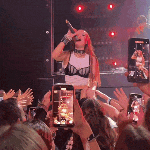 a woman singing into a microphone while a crowd takes pictures
