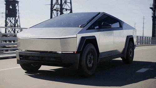a silver tesla cybertruck is driving down a bridge