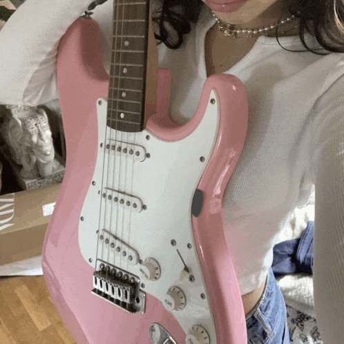 a woman is holding a pink electric guitar with a white pickguard