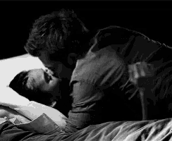 a black and white photo of a man kissing a woman in bed .