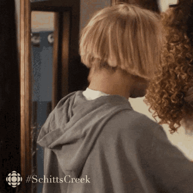 a man in a grey hoodie is standing in front of a mirror with #schitts creek written on the bottom
