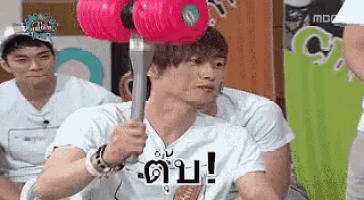 a man in a white shirt is holding a pink dumbbell on his head .