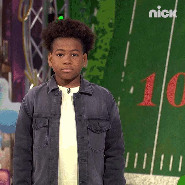 a young boy in a denim jacket stands in front of a green field with the number 10 on it