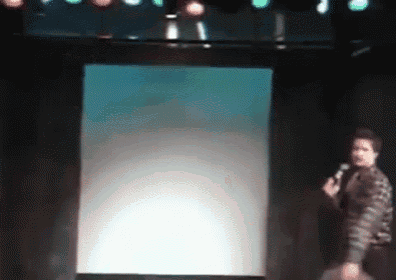 a man stands on a stage holding a microphone in front of a screen