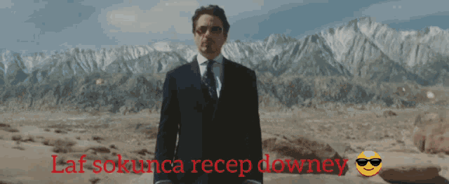 a man in a suit and tie stands in a desert with the words laf sokunca recep downey written below him