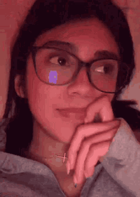 a girl wearing glasses and a cross necklace is looking at the camera .